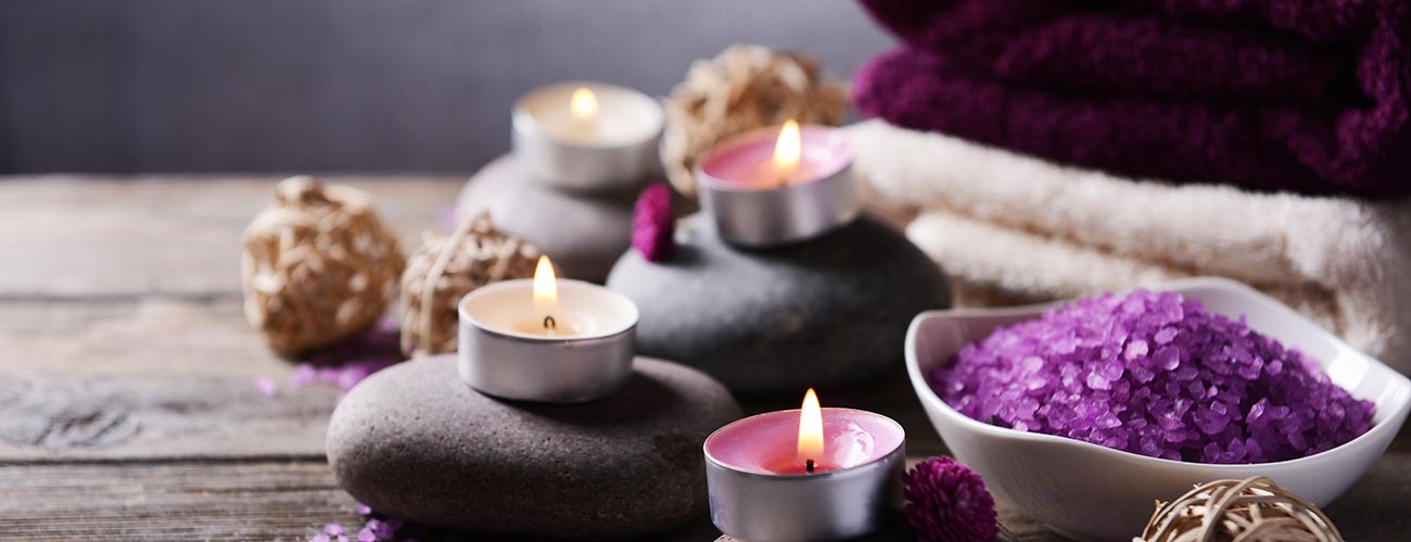 Schwarze Steine mit brennenden Kerzen und violette Kristalle als Dekoration des Wellnessbereiches