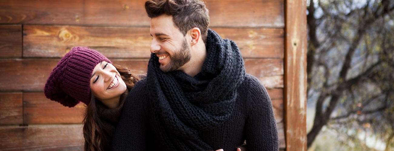 Verliebtes Paar mit dicken Pullovern vor einer Holzhütte im Winter