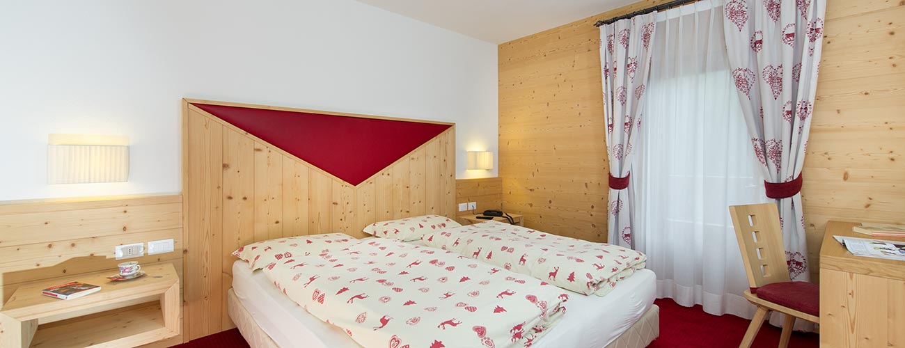 Camera dell'Hotel Gran Mugon con decori in legno e tappezzeria rossa