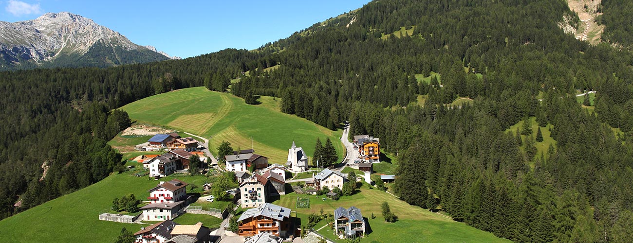 The Hotel Gran Mugon surrounded by woods on a hill in Vigo di Fassa