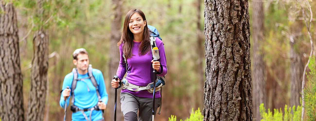 Couple with hiking poles while hiking in the woods around Vigo di Fassa