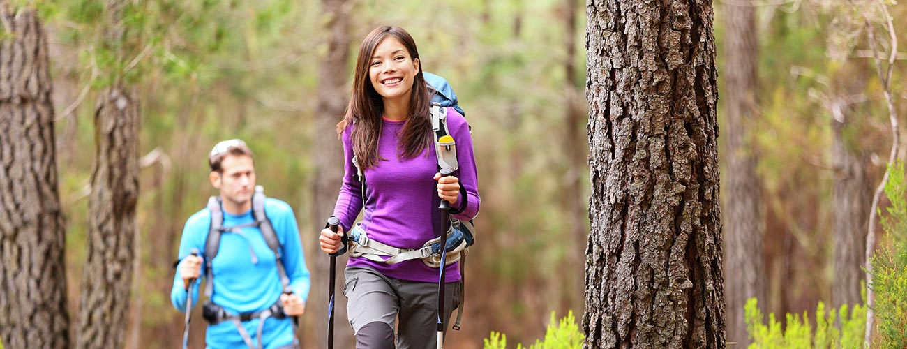 Paar mit Wanderstöcken beim Wandern im Wald rund um Vigo di Fassa